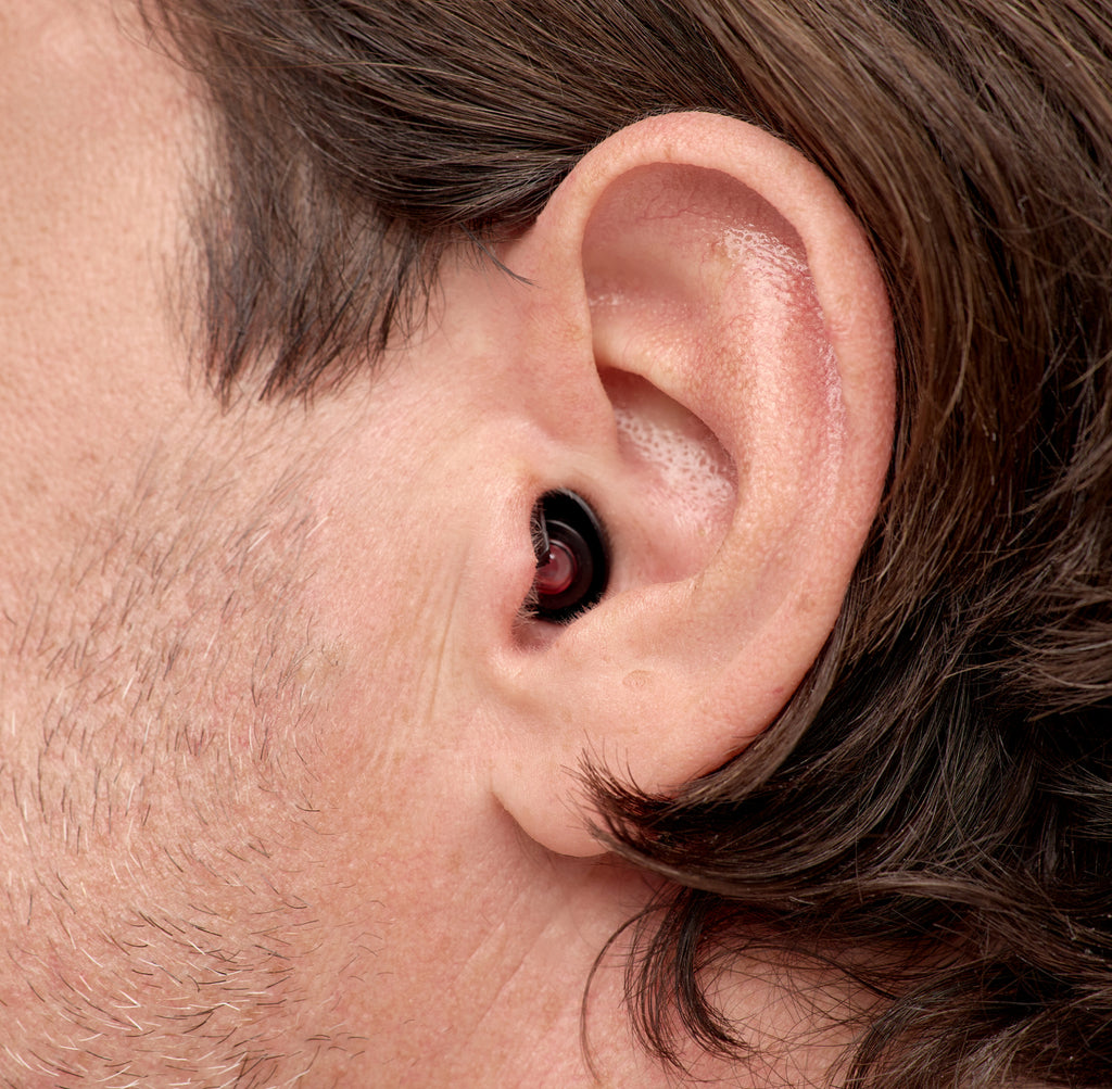 Nahaufnahme eines Ohrs mit diskretem, ergonomisch geformtem schwarzen Ohrstöpsel. Der Ohrstöpsel sitzt sicher und bequem im Ohr und bietet unauffälligen Schutz und Komfort.