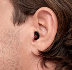 Nahaufnahme eines Ohrs mit diskretem, ergonomisch geformtem schwarzen Ohrstöpsel. Der Ohrstöpsel sitzt sicher und bequem im Ohr und bietet unauffälligen Schutz und Komfort.