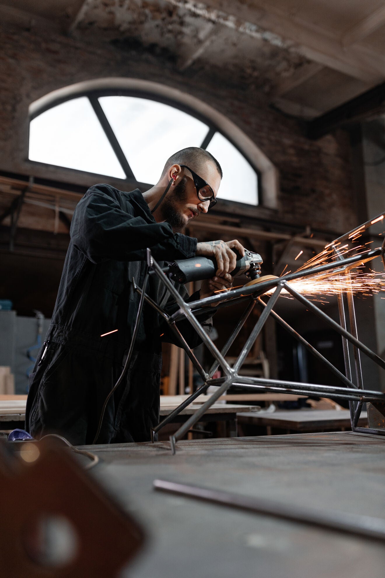Industriearbeiter mit Schutzbrille und gelben Gehörschutzstöpseln beim Schleifen von Metall. Zertifizierter Industrie Gehörschutz für Arbeitsschutz, Lärmschutz und sichere Arbeitsumgebungen.