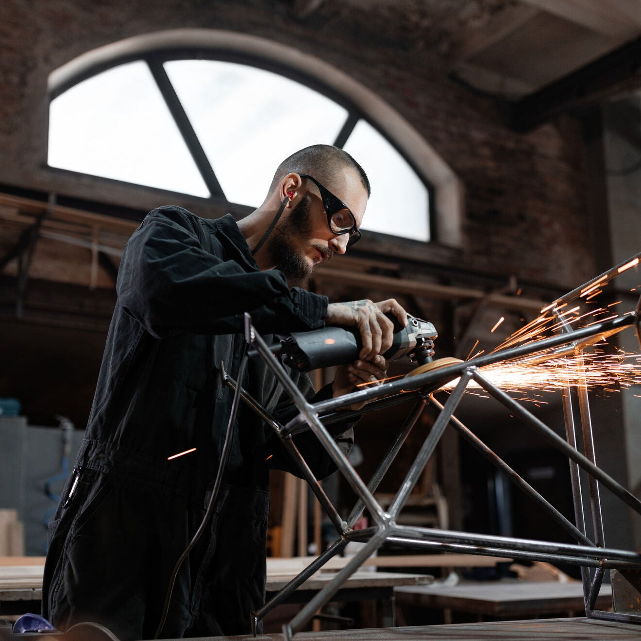 Industriearbeiter mit Schutzbrille und gelben Gehörschutzstöpseln beim Schleifen von Metall. Zertifizierter Industrie Gehörschutz für Arbeitsschutz, Lärmschutz und sichere Arbeitsumgebungen.