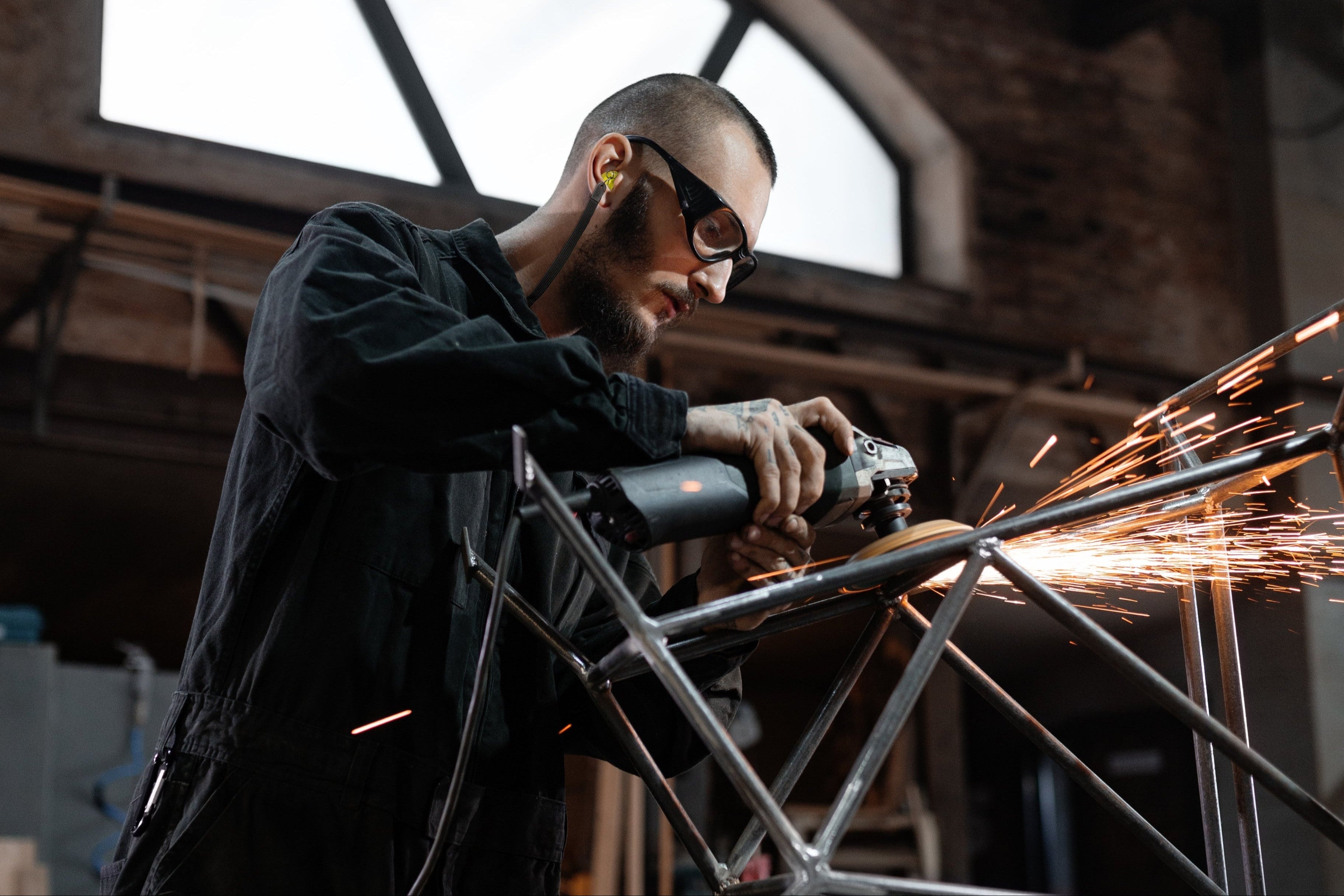 Industriearbeiter mit Schutzbrille und gelben Gehörschutzstöpseln beim Schleifen von Metall. Zertifizierter Industrie Gehörschutz für Arbeitsschutz, Lärmschutz und sichere Arbeitsumgebungen.
