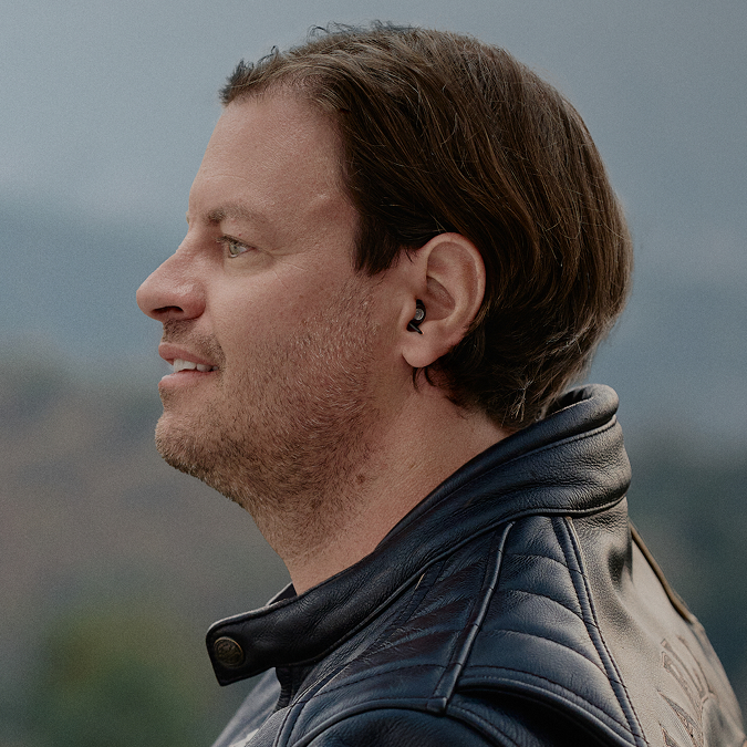 Mann trägt schwarze Ohrstöpsel beim Motorradfahren. Die Ohrstöpsel schützen effektiv vor Wind- und Motorengeräuschen, ermöglichen aber weiterhin die Wahrnehmung wichtiger Umgebungsgeräusche. Ideal für entspannte und sichere Fahrten.