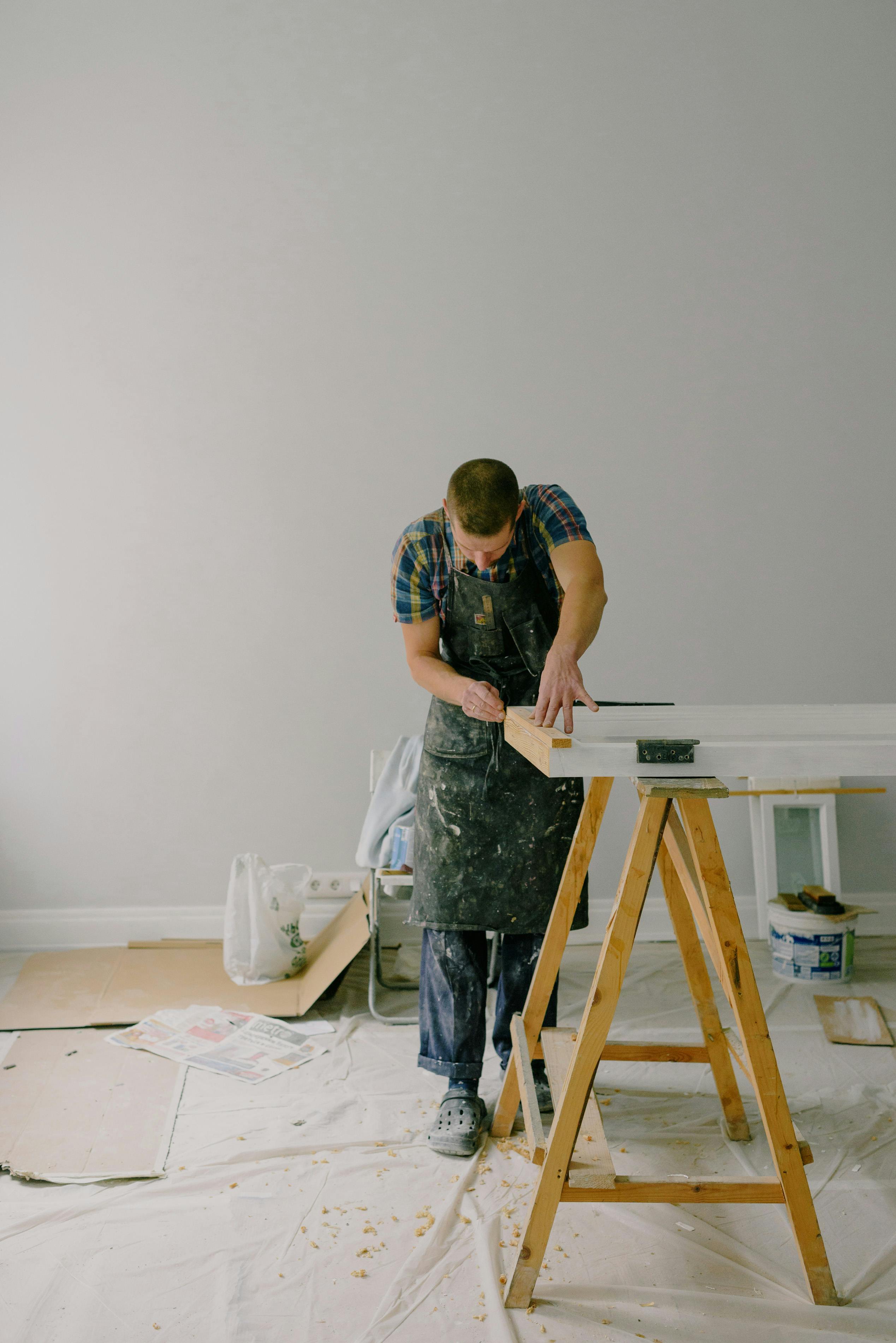 Handwerker in Schürze arbeitet konzentriert an einem Holzstück in einem hellen Raum mit Werkzeugen.